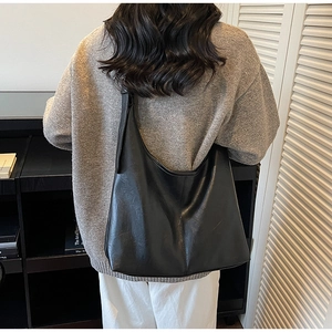 Rear view of model wearing a large black PU leather tote bag with wide shoulder strap