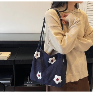 Detail of blue knitted tote bag with floral pattern and slim shoulder straps on model