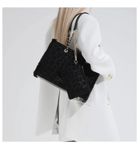 Dettaglio della borsa tote leopardata nera con catena dorata indossata su un abito bianco