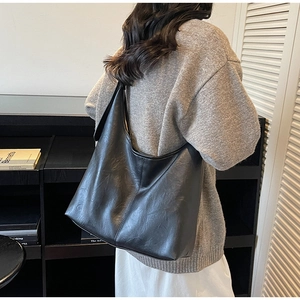 Side view of large black leather hobo bag on shoulder showing matte lychee grain and stitching