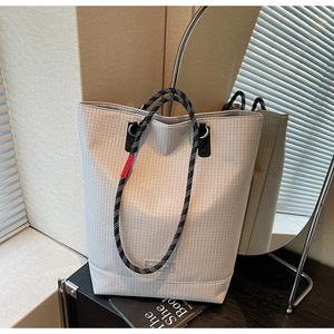 Detail of grey checkered tote bag with woven rope handles and red decorative tag