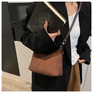 Nahaufnahme der braunen Wildledertasche mit goldenem Logo und dunklem Lederriemen