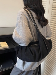 Minimalist black suede crescent tote bag shown on model in a stylish indoor setting