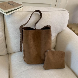 Detail view of brown suede bucket bag with matching pouch and wide woven strap on a sofa