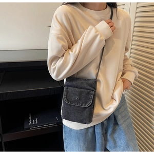 Detail of a minimalist black denim crossbody bag with a round metal snap button and flap