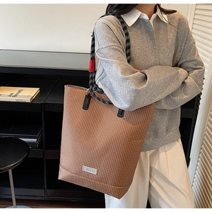 Close-up of brown plaid tote bag with braided rope handle and metal brand logo detail