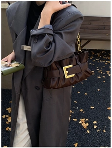 Detail of a pleated dark coffee leather bag with a bold gold buckle and chain strap