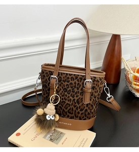 Detail of leopard print bucket bag with brown leather trim and plush charm on a table