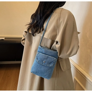 Close-up of a blue denim mini crossbody bag with metal buckle on a khaki trench coat