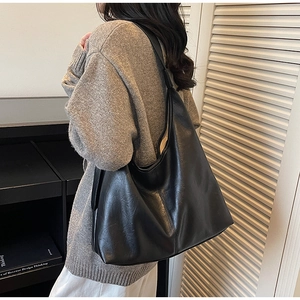 Side view of a large black leather hobo shoulder bag paired with a gray knit sweater