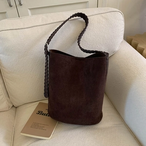 Detail of dark brown suede bucket bag with woven strap on a white fabric sofa
