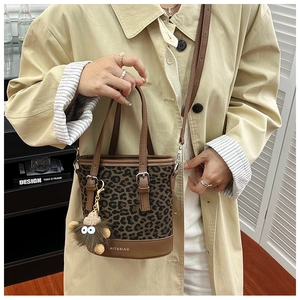 Detailed view of leopard print bucket bag with leather handles and plush monster charm