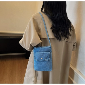 Detailed view of light blue denim crossbody bag worn by model in minimalist indoor setting