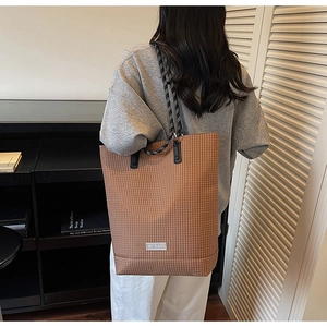 Close-up of brown checkered tote bag featuring stylish thick rope handles on shoulder