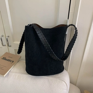 Detail of black suede bucket bag featuring a unique wide woven shoulder strap on sofa