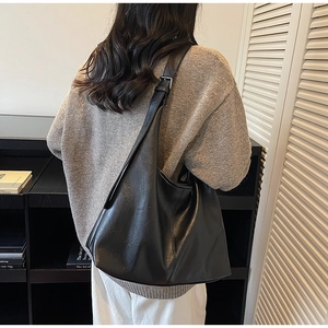 Detailed view of black pebbled leather tote bag worn by model in a minimalist modern setting