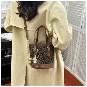 Close-up of leopard print bucket bag with leather trim and decorative plush pendant