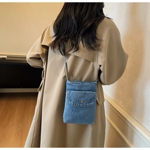 Detail of light blue denim crossbody phone bag showing texture and metal button on model
