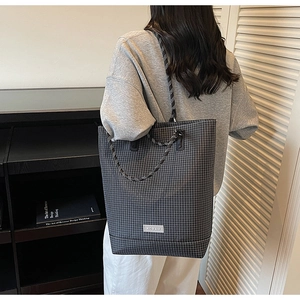 Detail of grey checkered tote bag featuring round rope handles and brand patch