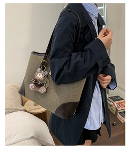 Dettaglio borsa tote leopardata con finiture in pelle marrone e ciondolo orsetto peluche