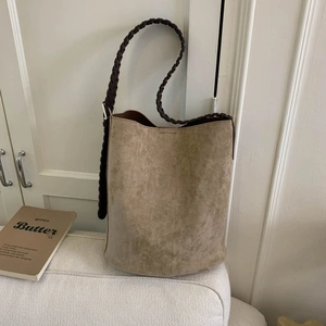 Close-up of khaki suede bucket bag featuring a brown braided shoulder strap and metal buckle
