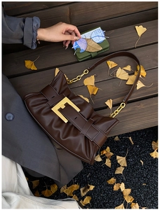 Detail of dark brown pleated underarm bag with gold buckle on wooden bench with ginkgo leaves