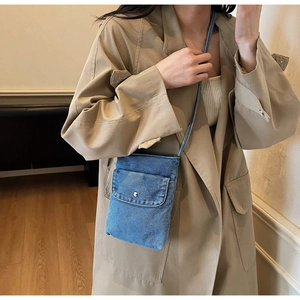 Blue denim crossbody bag with flap pocket and button shown on a model in trench coat