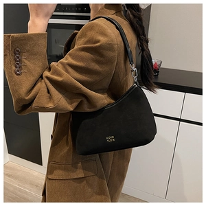 Detail der schwarzen Wildleder-Hobotasche mit Silberbeschlägen auf braunem Cord-Blazer