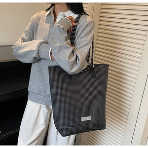 Detail of grey plaid tote bag with rope handles and logo patch in casual setting