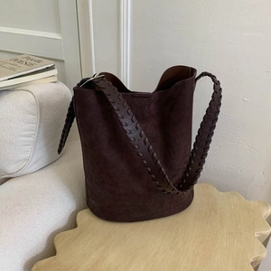 Detail of dark brown suede bucket bag featuring a decorative woven shoulder strap
