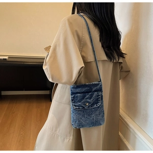Detail of blue washed denim crossbody bag featuring a metal snap button on front pocket