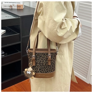 Close-up of stylish leopard print bucket bag with leather handles on a beige coat outfit