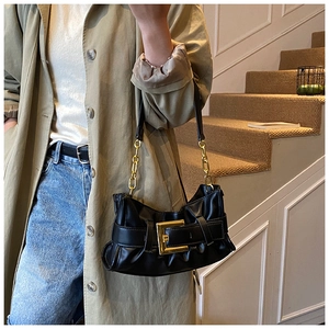 Detail of black pleated shoulder bag featuring a large gold square buckle and chain strap