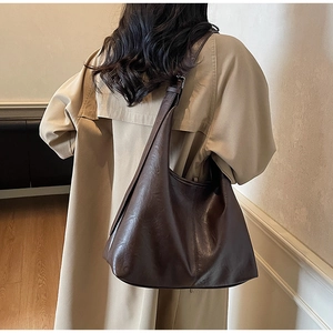 Detail of deep brown leather tote bag showing drape and texture on a model's shoulder