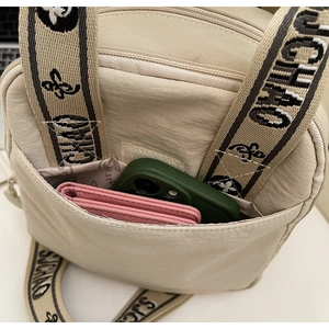 Détail du sac bandoulière en nylon beige montrant la poche avant avec velcro et sangle