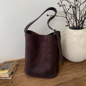 Detail of dark brown suede bucket bag with woven strap on a minimalist wooden bench
