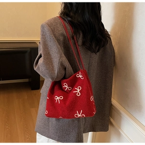 Vue détaillée du sac en laine rouge avec motif nœud blanc sur l'épaule d'un mannequin