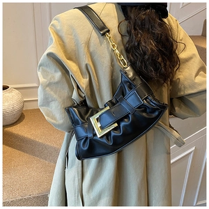 Detail of black pleated underarm bag featuring large gold buckle and metal chain strap