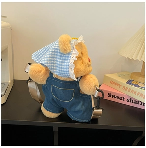 Detail of plush yellow bear backpack in denim overalls with a lace sun hat and strap