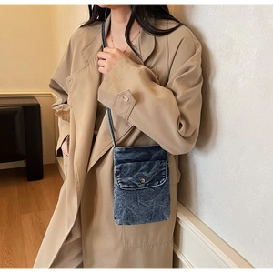 Lifestyle shot of a mini blue denim phone crossbody bag styled with a khaki trench coat