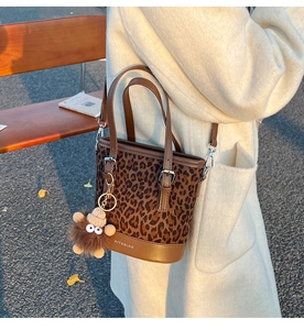 Close-up of leopard print bucket bag with plush charm and logo in autumn light