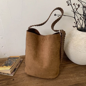 Detailed view of dark brown suede bucket bag featuring a wide woven shoulder strap and metal buckle