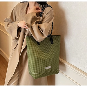 Detail of green checkered canvas tote bag with woven rope handles and brand logo tag