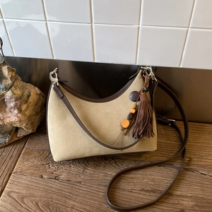 Detail of khaki suede hobo bag with retro fringes and beaded charms on wooden surface