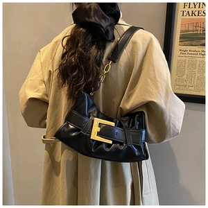 Close-up of black pleated leather underarm bag with gold buckle on a model in a trench coat