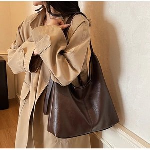 Detail of a large dark brown PU leather hobo bag worn with a chic beige trench coat