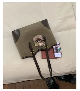 Dettaglio borsa tote in tela leopardata con spalline in pelle marrone e ciondolo di peluche