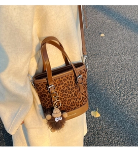 Detail view of leopard print bucket bag featuring brown leather trim and plush charm
