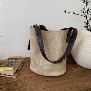 Detailed shot of retro suede bucket bag with brown woven leather strap on wooden surface