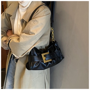 Detail view of black pleated underarm bag featuring a bold gold square buckle and chain strap